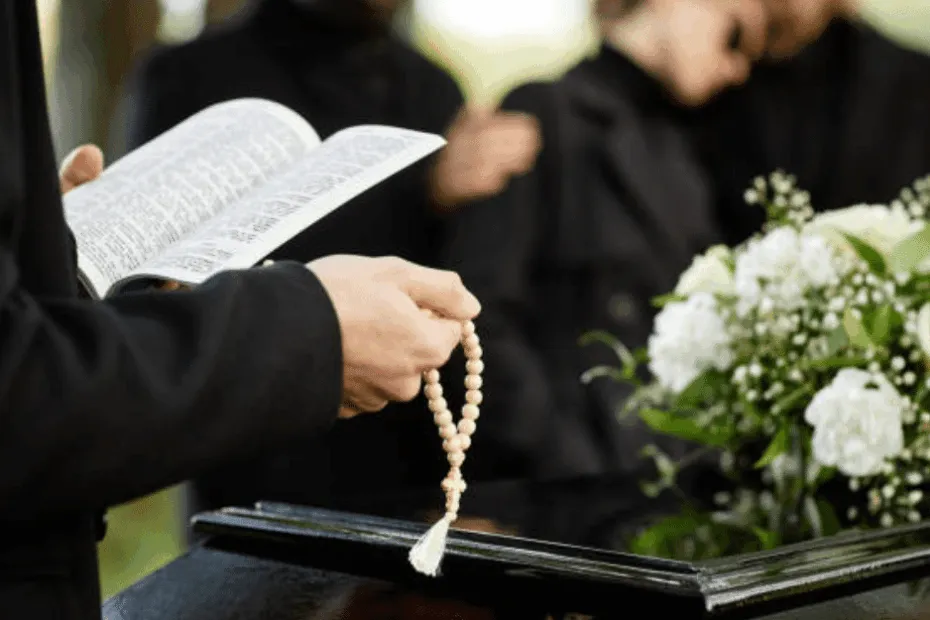 Prete con un rosario in mano legge una preghiera durante un funerale