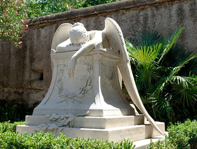 Statua di un angelo che poggia la fronte su un braccio poggiato su una lapide