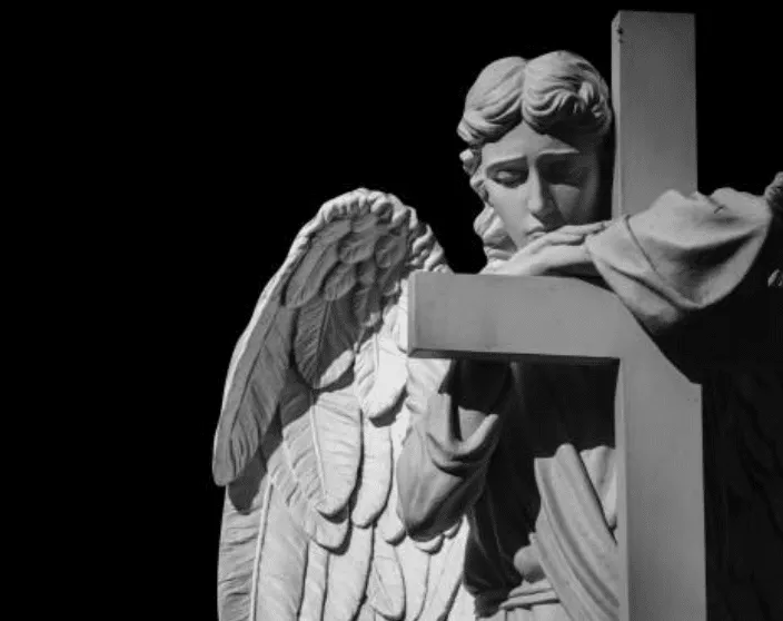 Statua di un angelo triste che abbraccia la croce