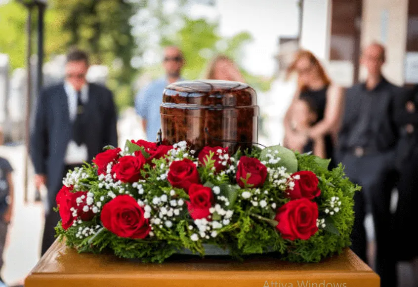 Urna cineraria con sullo sfondo un gruppo di persone in abito da funerale